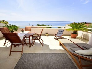 Une terrasse avec une table et des chaises, un fauteuil de relaxation et des plantes en pot.
