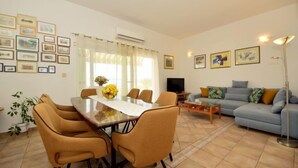 A living room with a dining table, chairs, a sofa, a TV, and framed pictures on the walls.