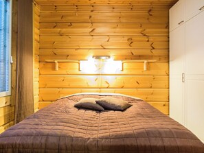 A wooden-paneled room with a bed, two wall-mounted lights, and a window with blinds.