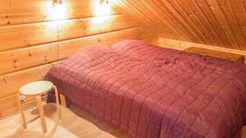 A single-bed room with a wooden ceiling and walls, a round wooden table, and a purple bedspread.