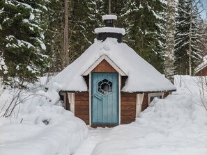 Eine schneebedeckte Holzhütte mit einer blauen Tür, umgeben von Schnee und Bäumen.