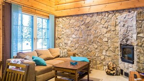 A cozy living room with a stone wall, a fireplace, and a wooden ceiling. - Rentotahko by Interhome (Nilsiä)