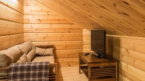 A cozy wooden cabin room with a sofa, a plaid blanket, and a television on a wooden stand. - Rentotahko by Interhome (Nilsiä)