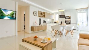 Una cocina moderna con armarios blancos, un comedor con sillas blancas y una sala de estar con un sofá y una mesa de centro.