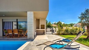 Un área de piscina moderna al aire libre con sillones de descanso y un conjunto de comedor.