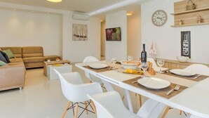 Una sala de estar moderna con un sofá, un comedor listo para cuatro personas y una cocina visible al fondo.