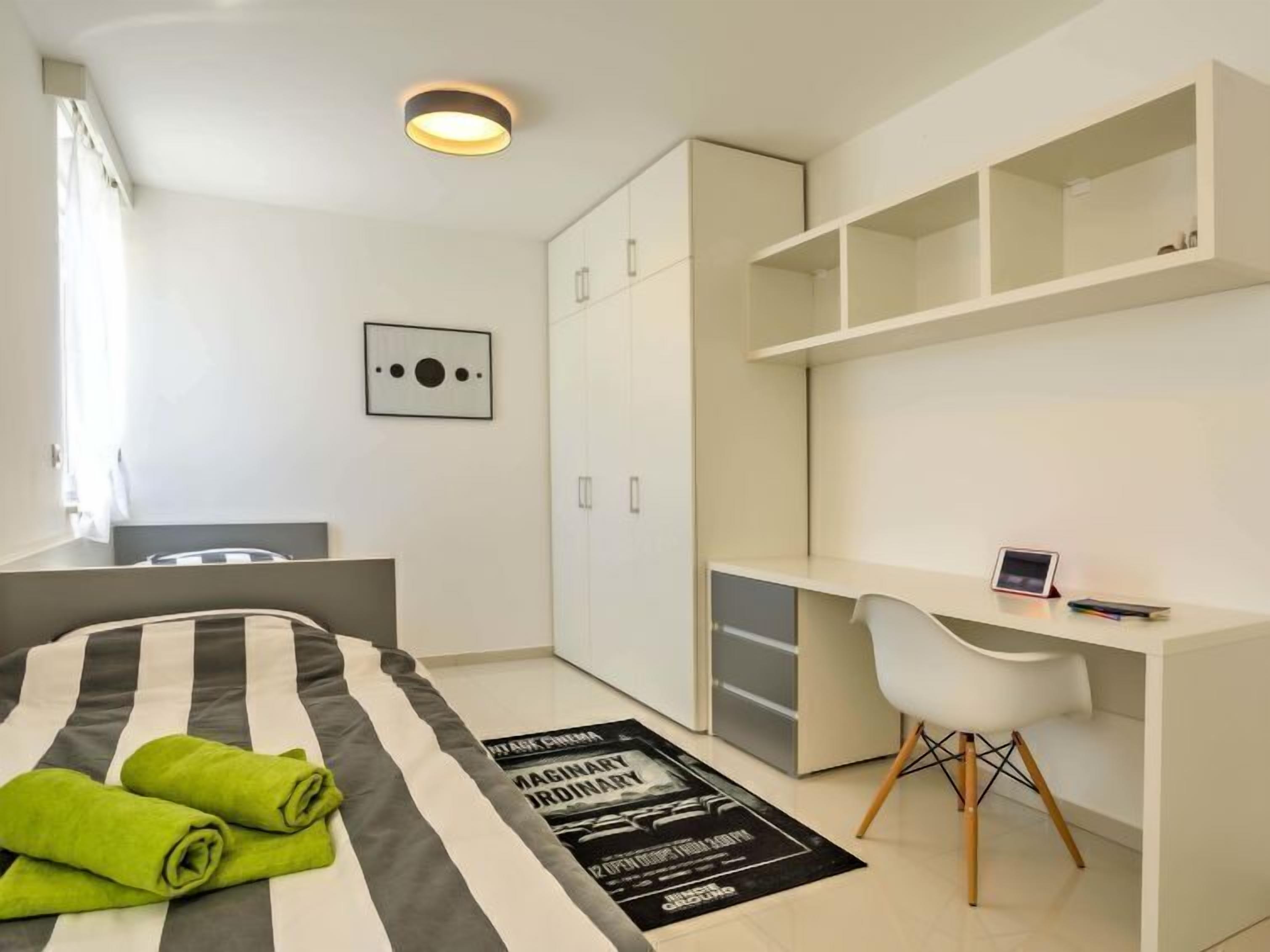 Une chambre moderne avec un lit, un bureau et une chaise. On y trouve également une armoire et une affiche accrochée au mur.