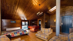 Een gezellig cabin interieur met een houten plafond, een bed met een kleurrijke quilt, een bank en een pooltafel.