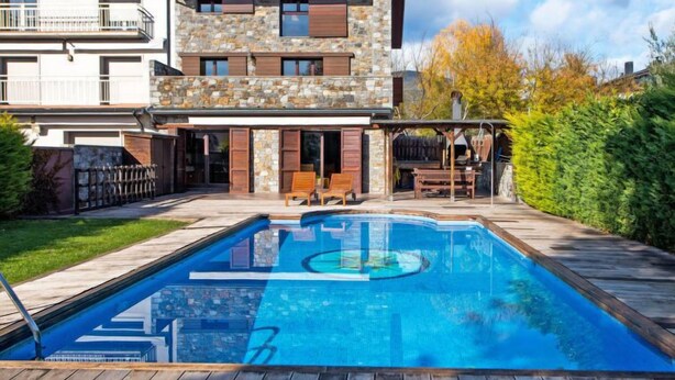 Een tweelaags huis met een gevel van natuursteen, een terras in de achtertuin en een zwembad.