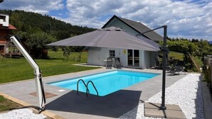A swimming pool with a covered patio area, a house in the background, and a clear sky. - Apartment Frank by Interhome (Feldkirchen in Kärnten)