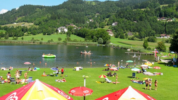 A lakeside resort with grassy areas, umbrellas, and people relaxing by the water. - Apartment Frank by Interhome (Feldkirchen in Kärnten)