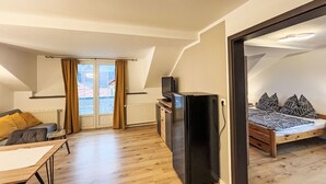 A modern loft bedroom with a wooden floor, a bed with patterned bedding, a black TV stand, and a view through a large window. - Apartment Frank by Interhome (Feldkirchen in Kärnten)