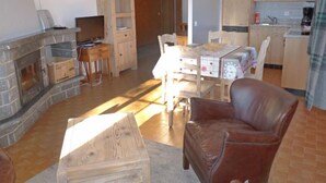 Een gezellige woonkamer met een stenen open haard, houten meubels, en een eethoek met een tafel en stoelen.