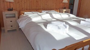 Een net opgemaakt bed met witte lakens, twee nachtkastjes met lampen en houten wanden.