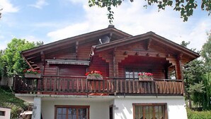 Een houten huis met twee verdiepingen, een balkon, witte muren en een klein terras.