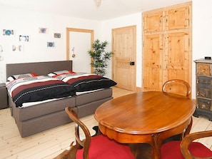 A room with a bed, a dining table, chairs, a wooden cabinet, and a door.
