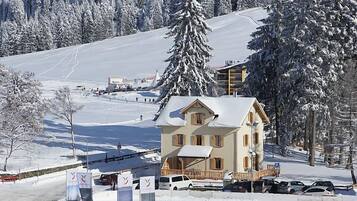 Un hôtel de style chalet, avec un toit enneigé, entouré d’une piste de ski et d’arbres.