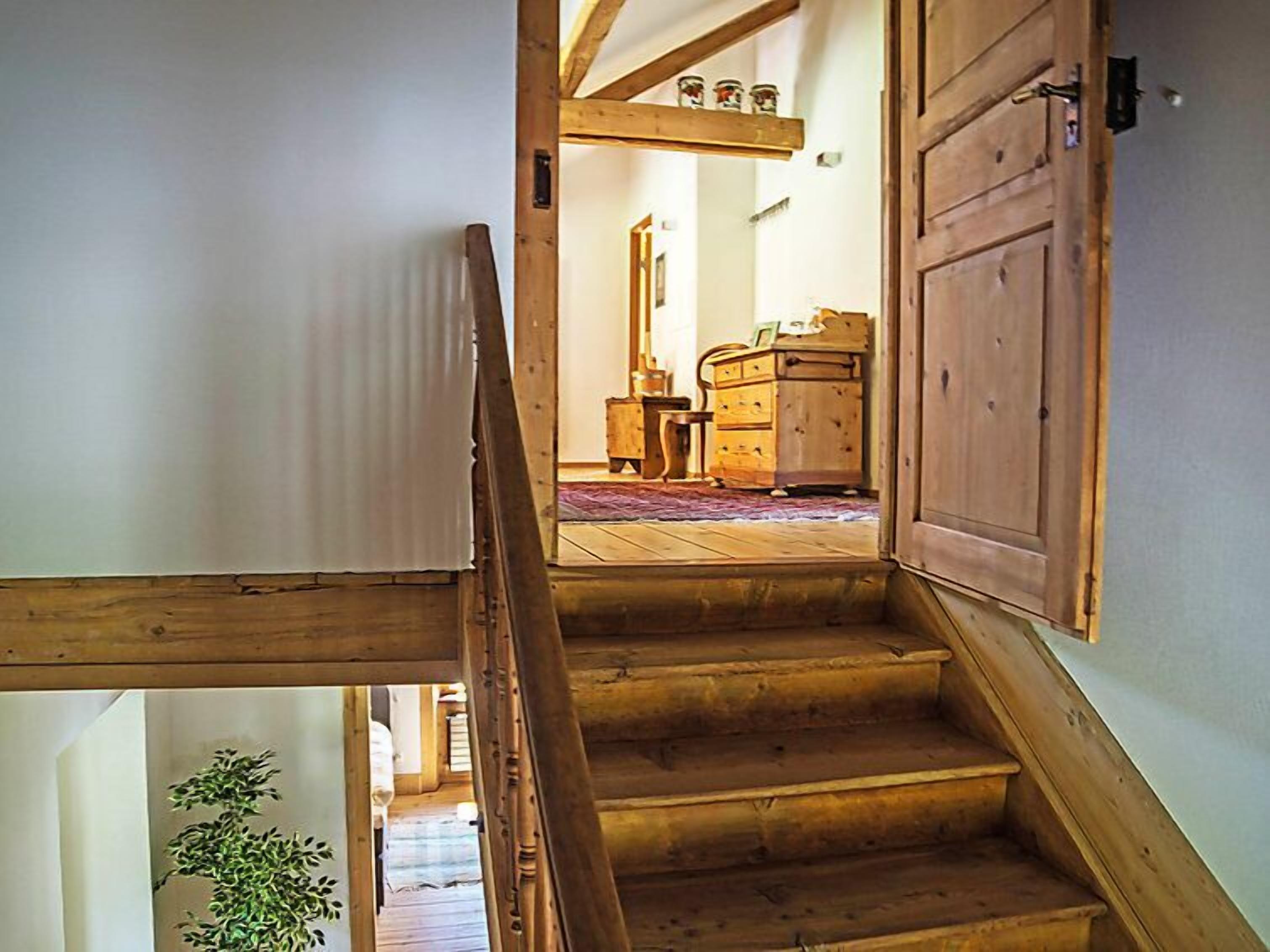 Un escalier en bois mène à une pièce où se trouvent une commode en bois et une petite table.