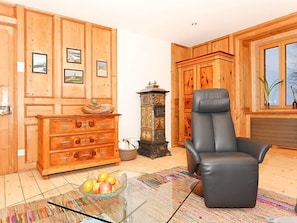 A wooden-paneled room with a leather chair, a glass coffee table with fruit, and a cabinet with decorative items.