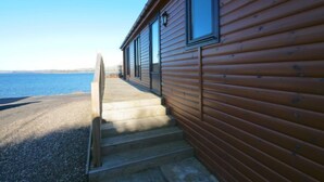 Une cabane en bois avec un escalier en béton menant à une porte, donnant sur une étendue d’eau.