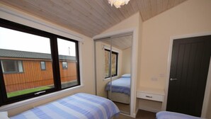 Une chambre avec deux lits, un miroir, une armoire et une fenêtre donnant sur un bâtiment en bois.