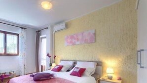 Een slaapkamer met een groot bed, een nachtkastje, een wandairconditioner en een raam met gordijnen.