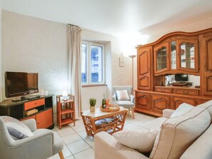 A living room with a sofa, a television, a wooden cabinet, and a dining table. - Mer et Soleil by Interhome (Carnac)