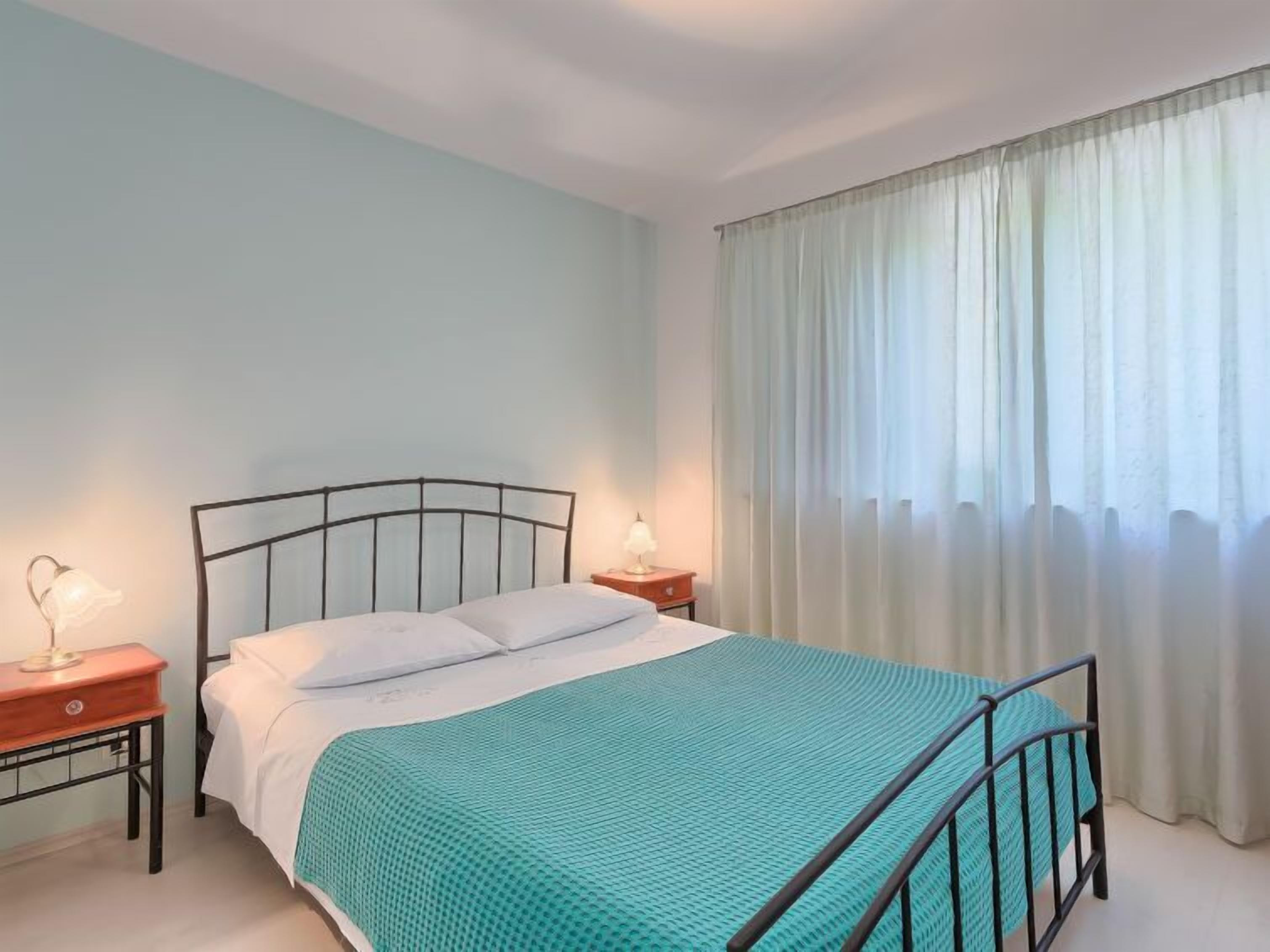 Ein Schlafzimmer mit einem Bett, zwei Nachttischen, einer Lampe und einem Fenster mit Vorhängen.