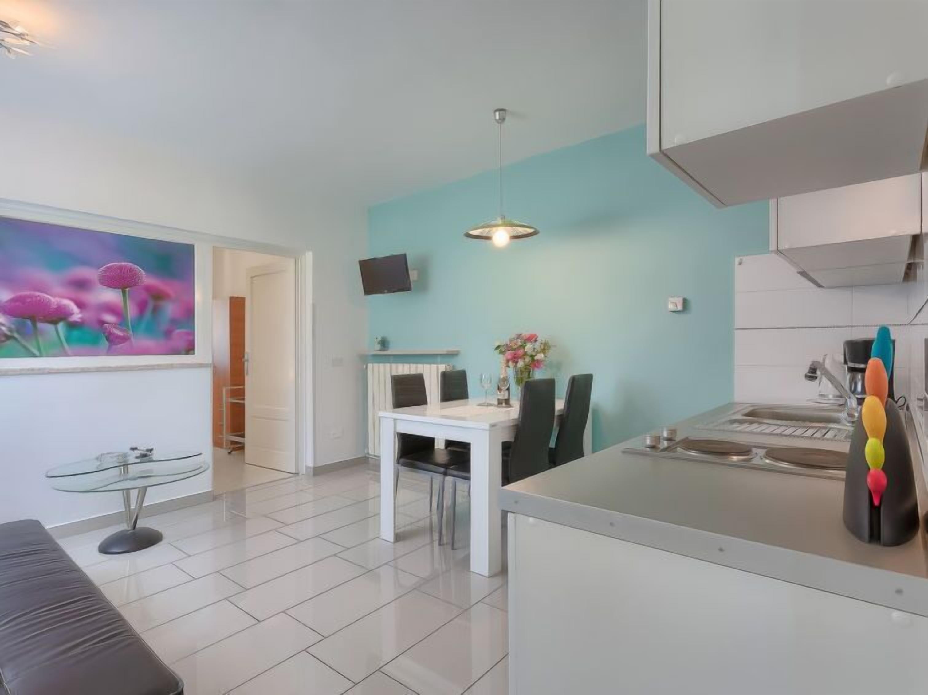 A modern kitchen with white cabinets, a dining area with a white table and chairs, and a pendant light.