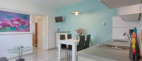 A modern kitchen with white cabinets, a dining area with a white table and chairs, and a pendant light.