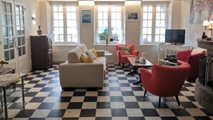 A living room with a checkered floor, a sofa, a red armchair, a television, and a fireplace. - La Congrière by Interhome (Cancale)