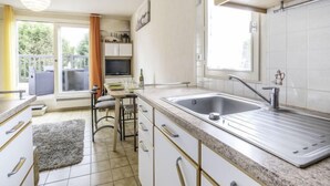 Una cocina moderna con armarios blancos, un lavamanos de acero inoxidable y una zona de comedor con mesa y sillas.