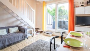 Una sala moderna con un sofá, una mesa de comedor para dos personas, una escalera y un televisor.