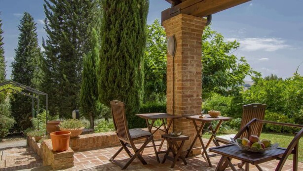Un patio al aire libre con columna de ladrillo, sillas de madera y una mesa.