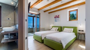 A modern bedroom with two green beds, a large window, and a bathroom with a sink and shower.