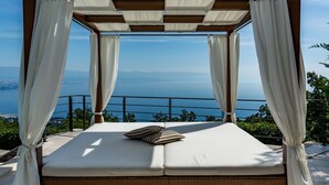 A bed with a canopy, a pillow, and a view of the sea.