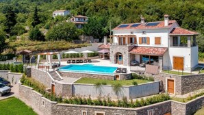 A two-story villa with a swimming pool, stone walls, and a view of the surrounding forest.