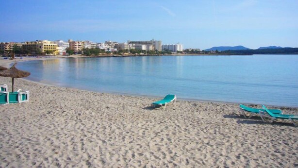 Ein Strand mit zwei grünen Liegestühlen und einem kleinen Poolbereich.