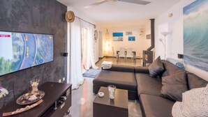 Ein modernes Wohnzimmer mit Flachbildfernseher, einer Couch, einem Couchtisch und einem Essbereich mit Stühlen und Tisch.