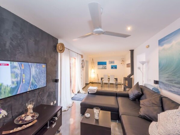 A modern living room with a flat-screen TV, a sofa, a coffee table, and a dining area with chairs and a table.