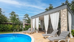 A pool area with lounge chairs and a stone building with a covered patio. - Vacation home Ofelia by Interhome (Buje)