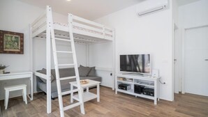 A bunk bed with a ladder, a TV, a small table, and a sofa in a room with wooden flooring. - Vacation home Ofelia by Interhome (Buje)