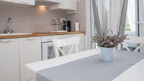 A modern kitchen with white cabinets, a wooden countertop, and a sink. There is a white table with a grey tablecloth and a potted plant. - Vacation home Ofelia by Interhome (Buje)