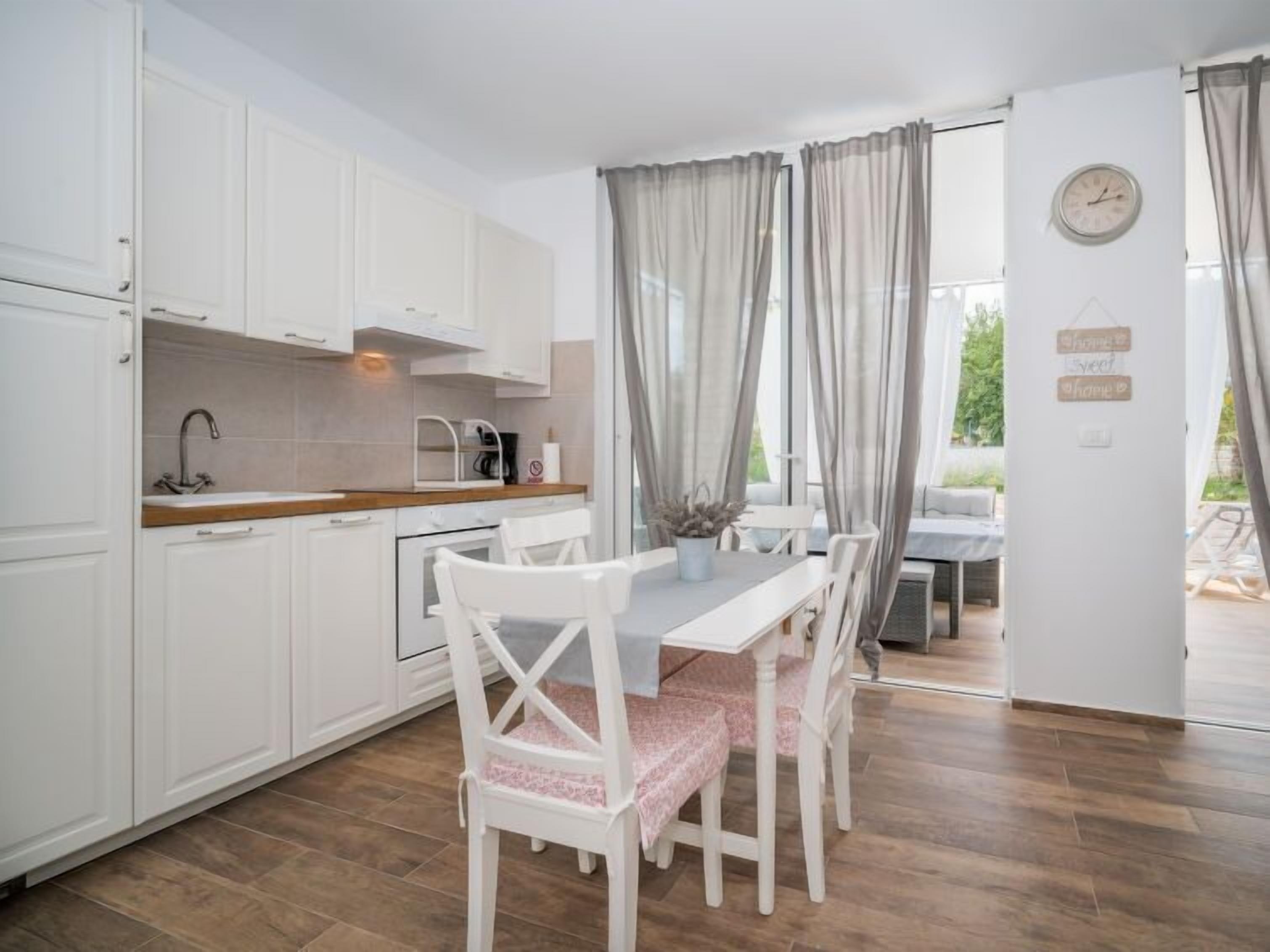 A compact kitchen with white cabinets, a wooden countertop, and a dining table with white chairs.
