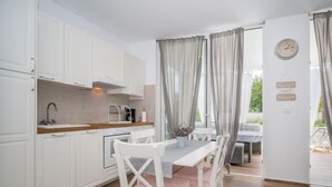 A compact kitchen with white cabinets, a wooden countertop, and a dining table with white chairs. - Vacation home Ofelia by Interhome (Buje)