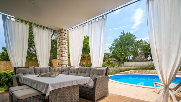 A covered patio area with a pool, wicker furniture, and white curtains. - Vacation home Ofelia by Interhome (Buje)