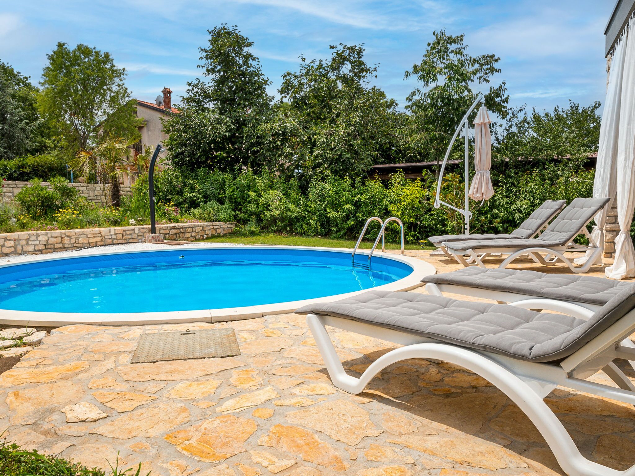 Une piscine dotée d’une plage en pierre, entourée de chaises longues et de verdure.