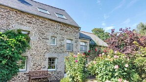 A stone building with a sloped roof, a wooden bench, and a garden with roses.