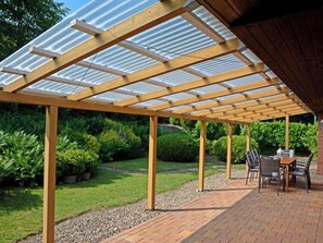 A covered patio area with a wooden pergola and a brick floor, surrounded by greenery. - Rosenhütte by Interhome (Extertal)