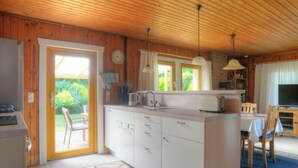 Une cuisine compacte avec des meubles blancs, un four encastré et un coin repas comprenant une table et des chaises.